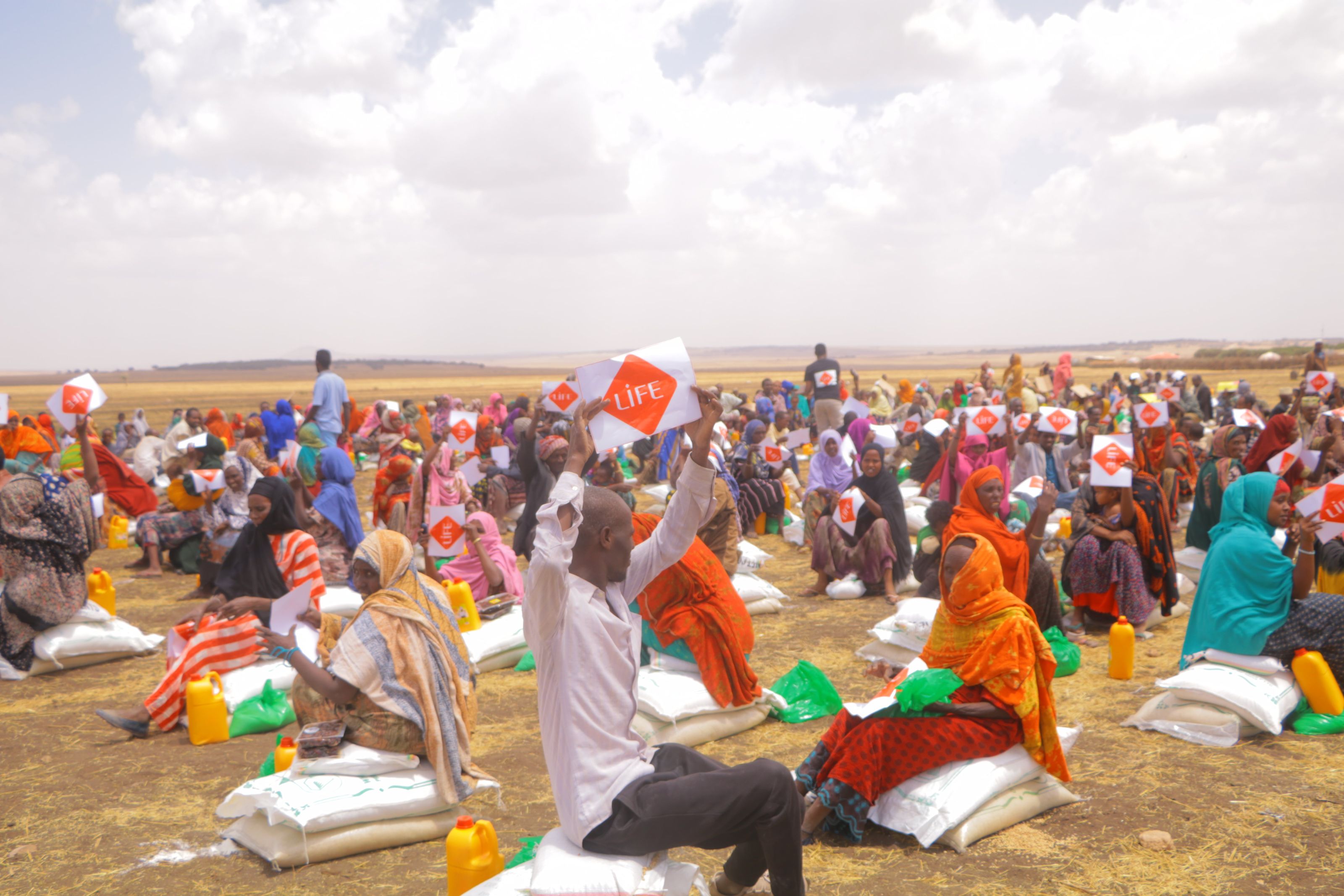 Des familles réunies en plein air brandissent leur fiche LIFE devant les sacs de vivres reçus lors d'une distribution en Éthiopie.