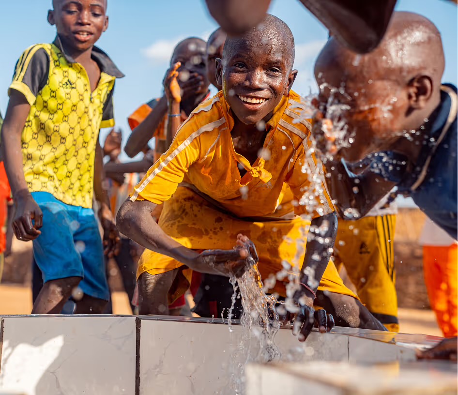 Des garçons rient en buvant et en s'aspergeant à la borne-fontaine d'eau potable construite par LIFE.