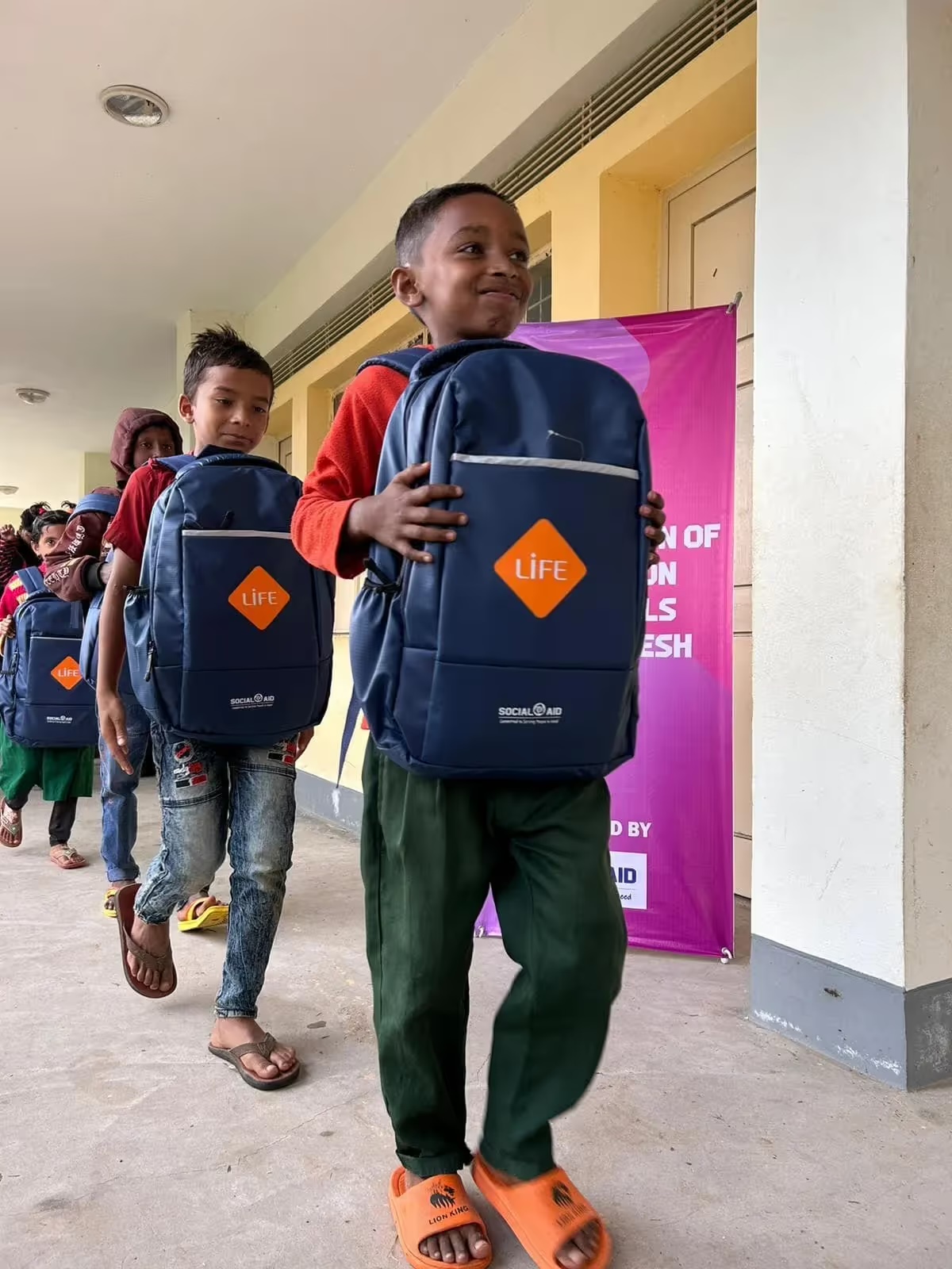 Des écoliers repartent en file avec le cartable neuf frappé du logo LIFE qu'ils viennent de recevoir au Bangladesh.