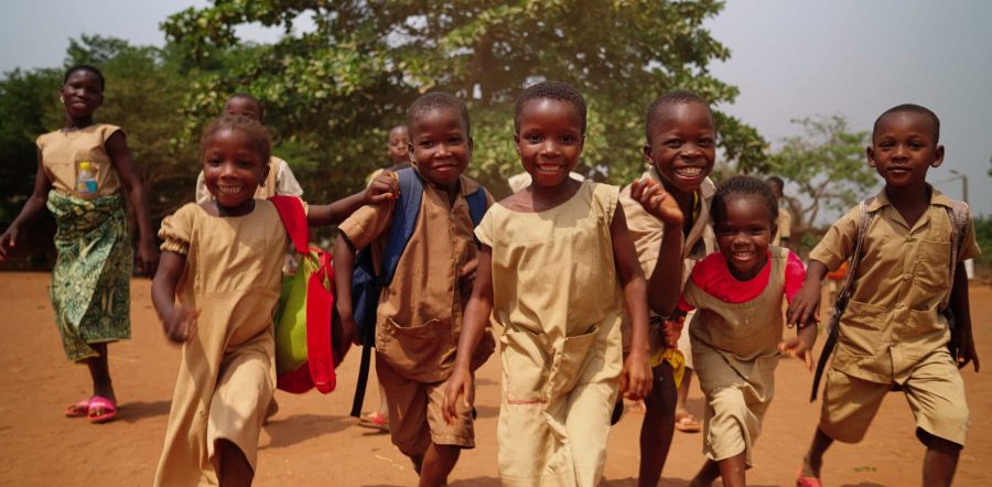 Des écoliers en uniforme beige courent en riant dans la cour de leur école au Togo.